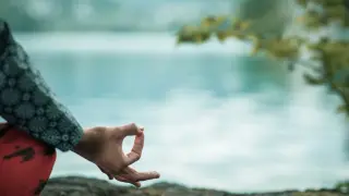 Dłoń w pozycji mudra na tle spokojnej wody.