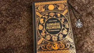 Książka "Słowiański przewodnik po świętowaniu" z bogatymi zdobieniami i naszyjnik z symbolem Słońca. Odkryj słowiańskie mantry i tradycje.
